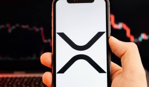 XRP cryptocurrency logo on the screen of smartphone in mans hand with downtrend on the chart