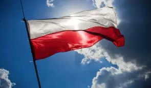 Polish national white and red flag waving against a bright blue sky and sunlit clouds.