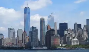 Lower Manhattan skyline in New York City featuring One World Trade Center viewed across the Hudson River under a blue sky.