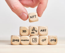Hand stacking an "NFT" wooden cube on blocks labeled with digital file formats like .jpeg, .gif, and .png.