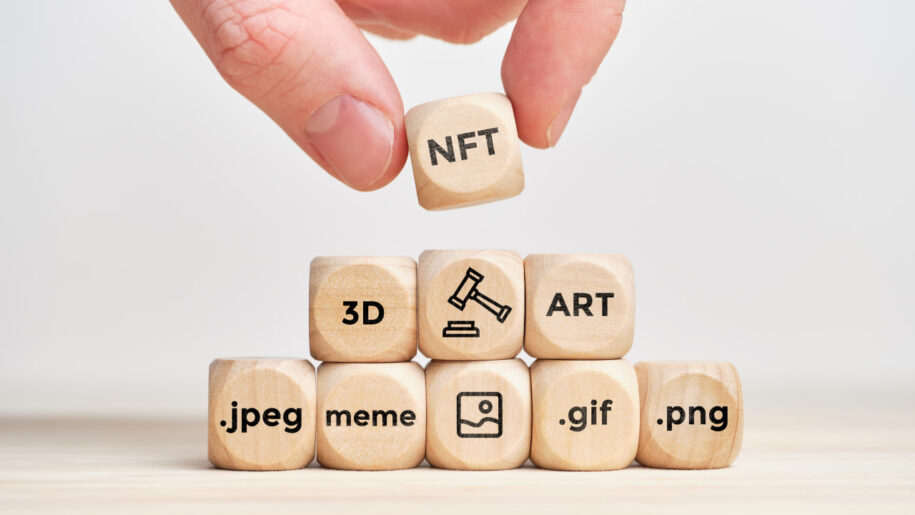 Hand stacking an "NFT" wooden cube on blocks labeled with digital file formats like .jpeg, .gif, and .png.