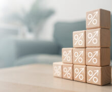 Wooden blocks with upward-arrow percentage symbols stacked in ascending steps, representing rising interest rates or growing yields.