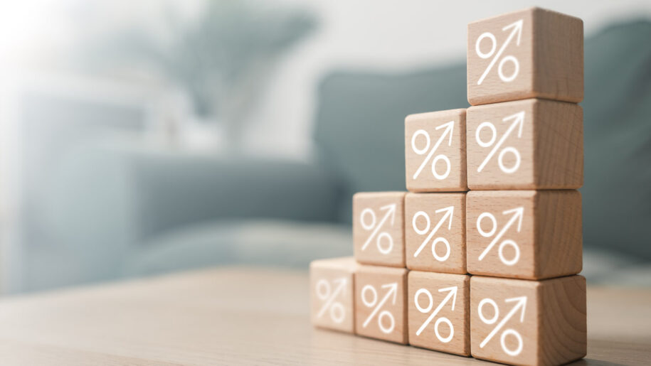 Wooden blocks with upward-arrow percentage symbols stacked in ascending steps, representing rising interest rates or growing yields.