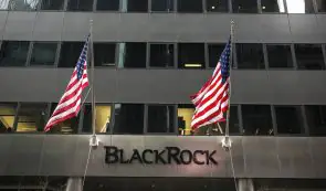 The exterior entrance of a BlackRock office building featuring the company signage and two American flags hanging on poles.