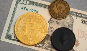 A gold Bitcoin token, a black Ethereum token, and a New York State souvenir token resting on top of a US dollar bill.