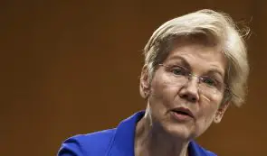 Portrait of US Senator Elizabeth Warren speaking during a congressional hearing in a blue blazer.