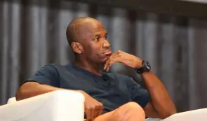 Arthur Hayes sitting on a panel stage and resting his chin on his hand during a conference.