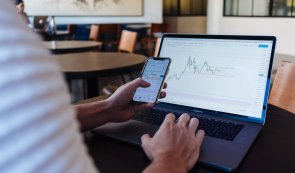 investor photo with laptop and mobile phone, looking at charts