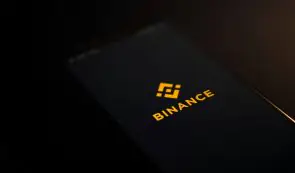 The Binance logo and wordmark displayed in yellow on the dark screen of a mobile phone.