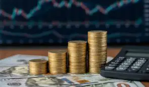 Stacks of gold coins arranged by height on dollar bills with a calculator and trading chart, symbolizing crypto staking rewards.
