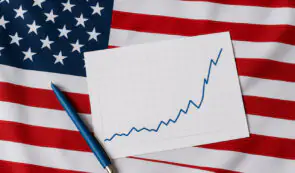 A paper chart displaying an upward-trending financial line and a blue pen resting on top of an American flag background.