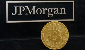 Physical Bitcoin coin displayed in front of a branded plaque with the JPMorgan corporate logo.