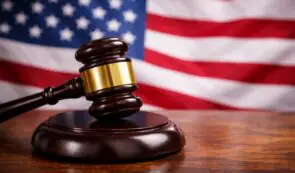 Wooden judge's gavel resting on a block with the United States flag in the background.