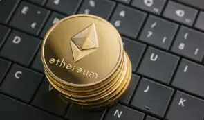 Stack of golden physical Ethereum tokens resting on a black laptop keyboard.