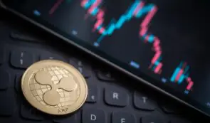 A physical gold XRP coin resting on a computer keyboard next to a smartphone displaying crypto price charts.