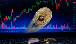 Gold Bitcoin coin in front of trading charts on laptop screen