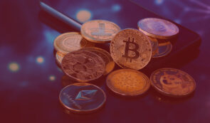 Group of physical cryptocurrency coins including Bitcoin, Ethereum, Ripple, Dogecoin, and Cardano, resting on a smartphone.