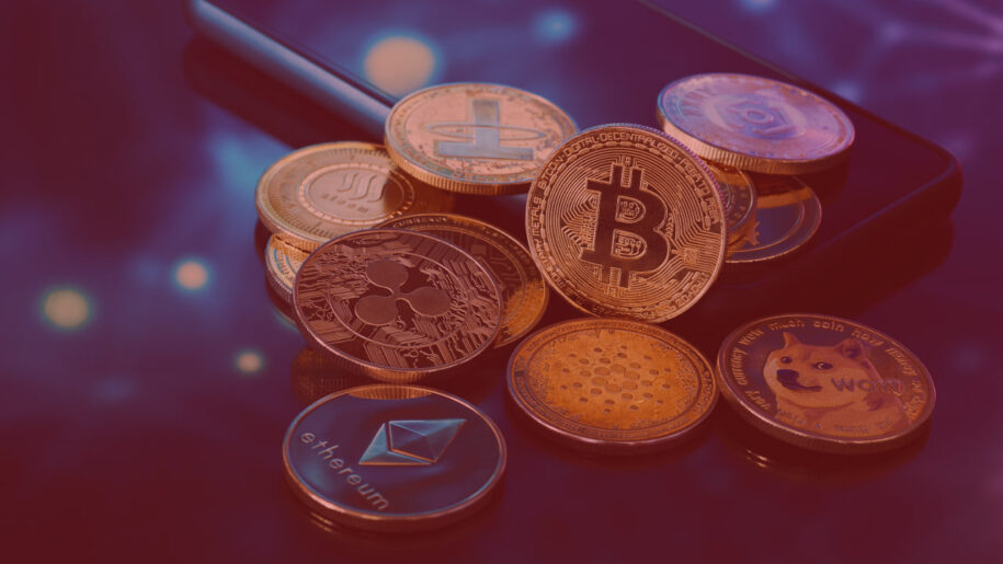 Group of physical cryptocurrency coins including Bitcoin, Ethereum, Ripple, Dogecoin, and Cardano, resting on a smartphone.