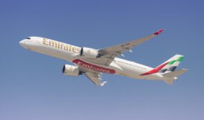 An Emirates passenger airplane in flight against a clear blue sky.